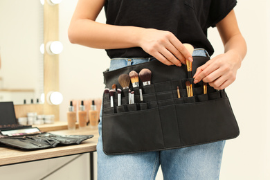 Photo of Professional makeup artist with belt organizer full of tools working in studio, closeup