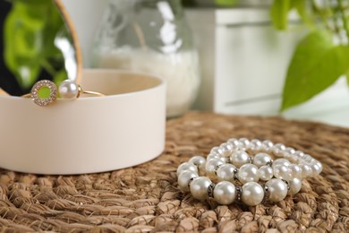 Photo of Stylish jewelry with pearls and box on wicker mat, closeup