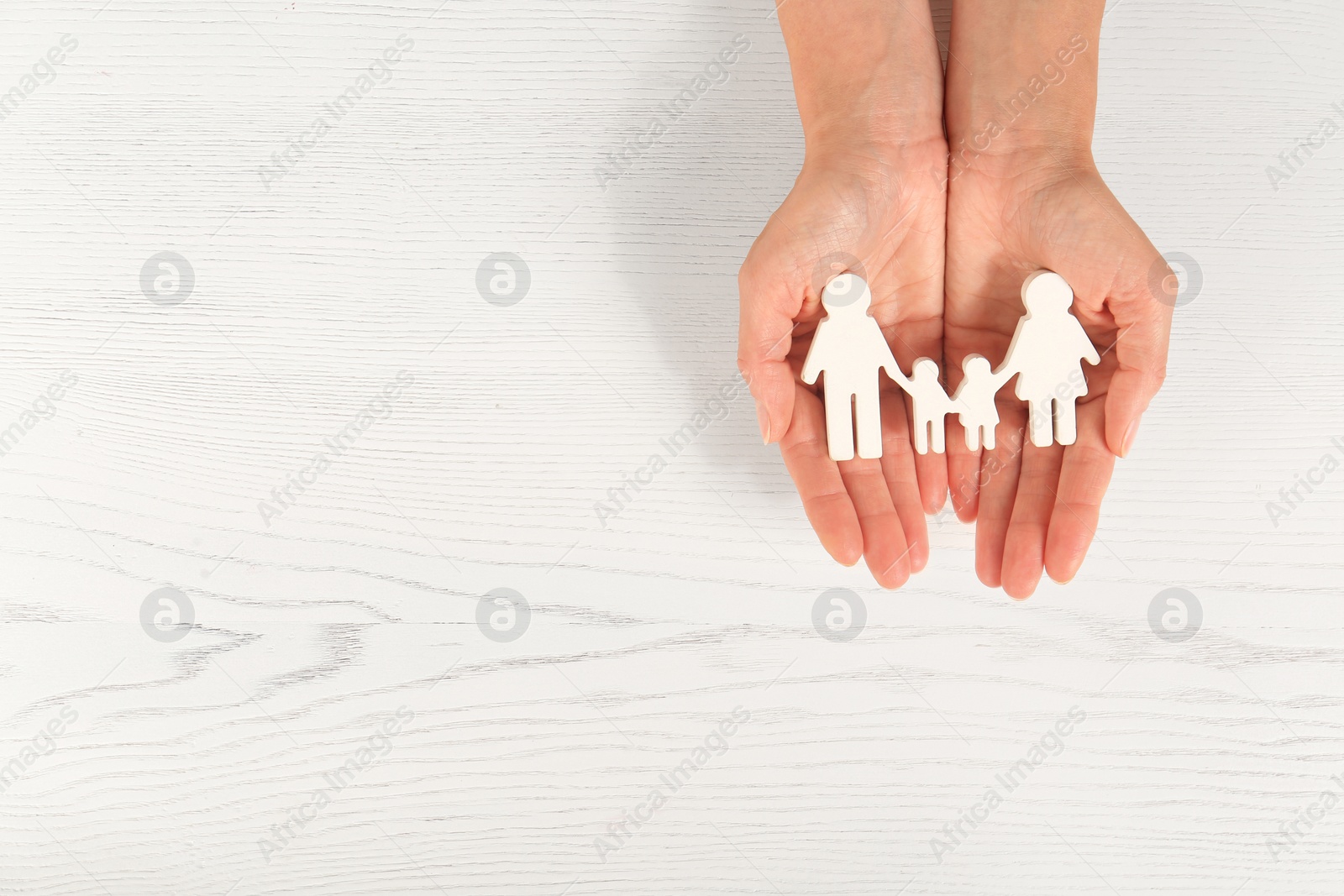 Photo of Woman holding figures of family in hands on white wooden background, top view. Space for text