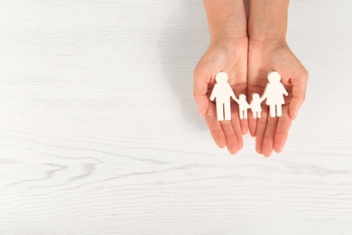 Woman holding figures of family in hands on white wooden background, top view. Space for text