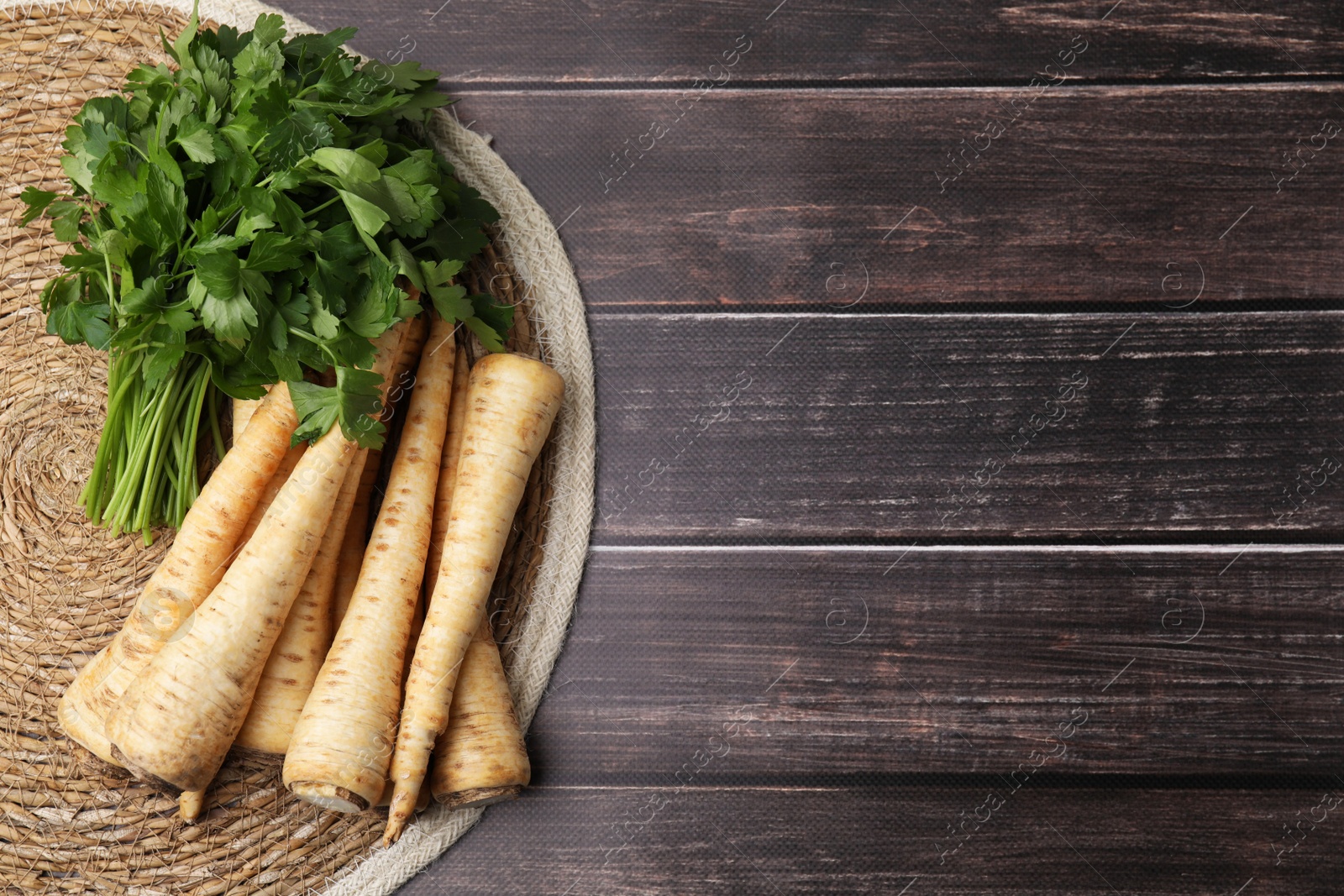 Photo of Raw parsley roots and bunch of fresh herb on wooden table, flat lay. Space for text