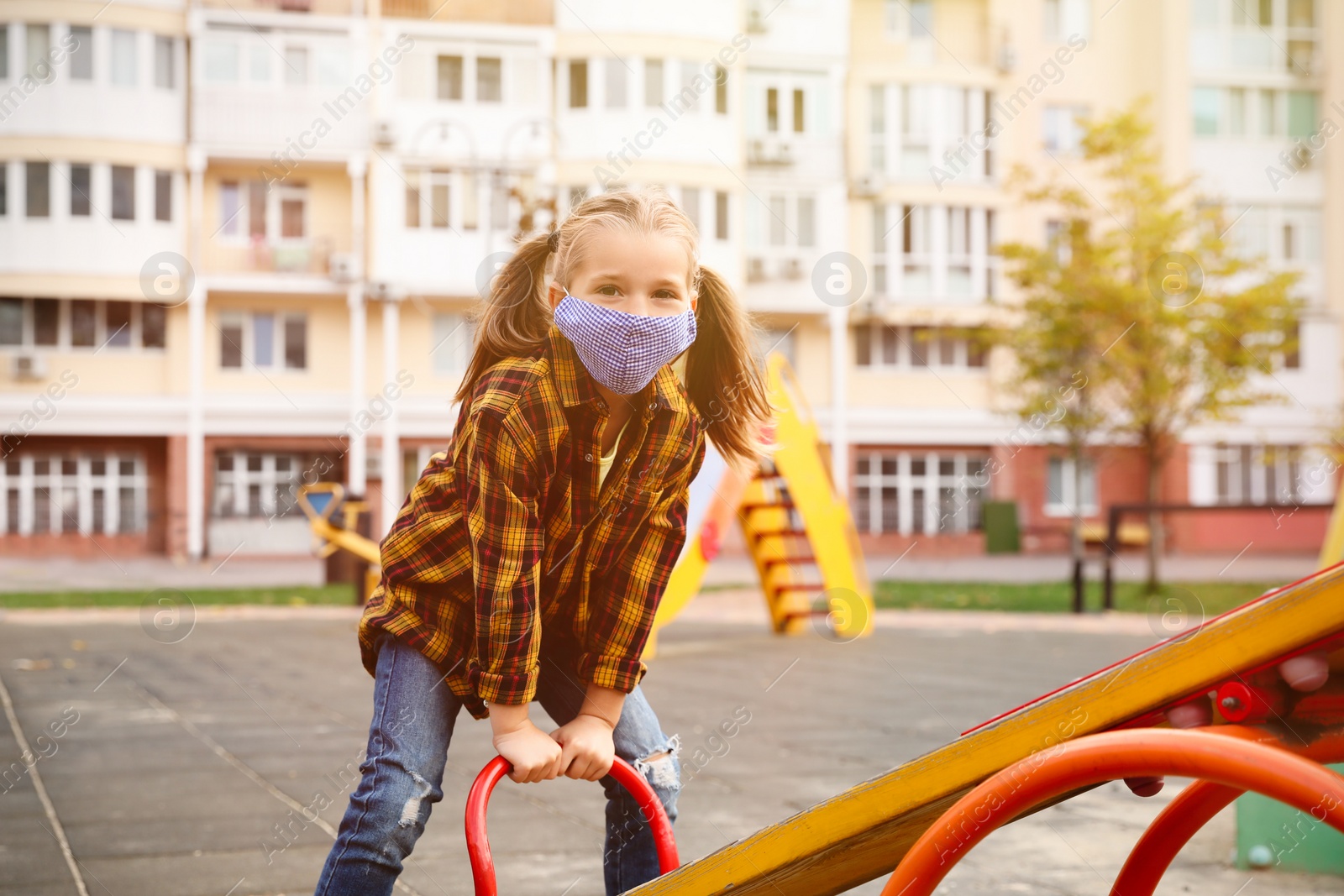 Photo of Little girl with medical face mask on playground during covid-19 quarantine