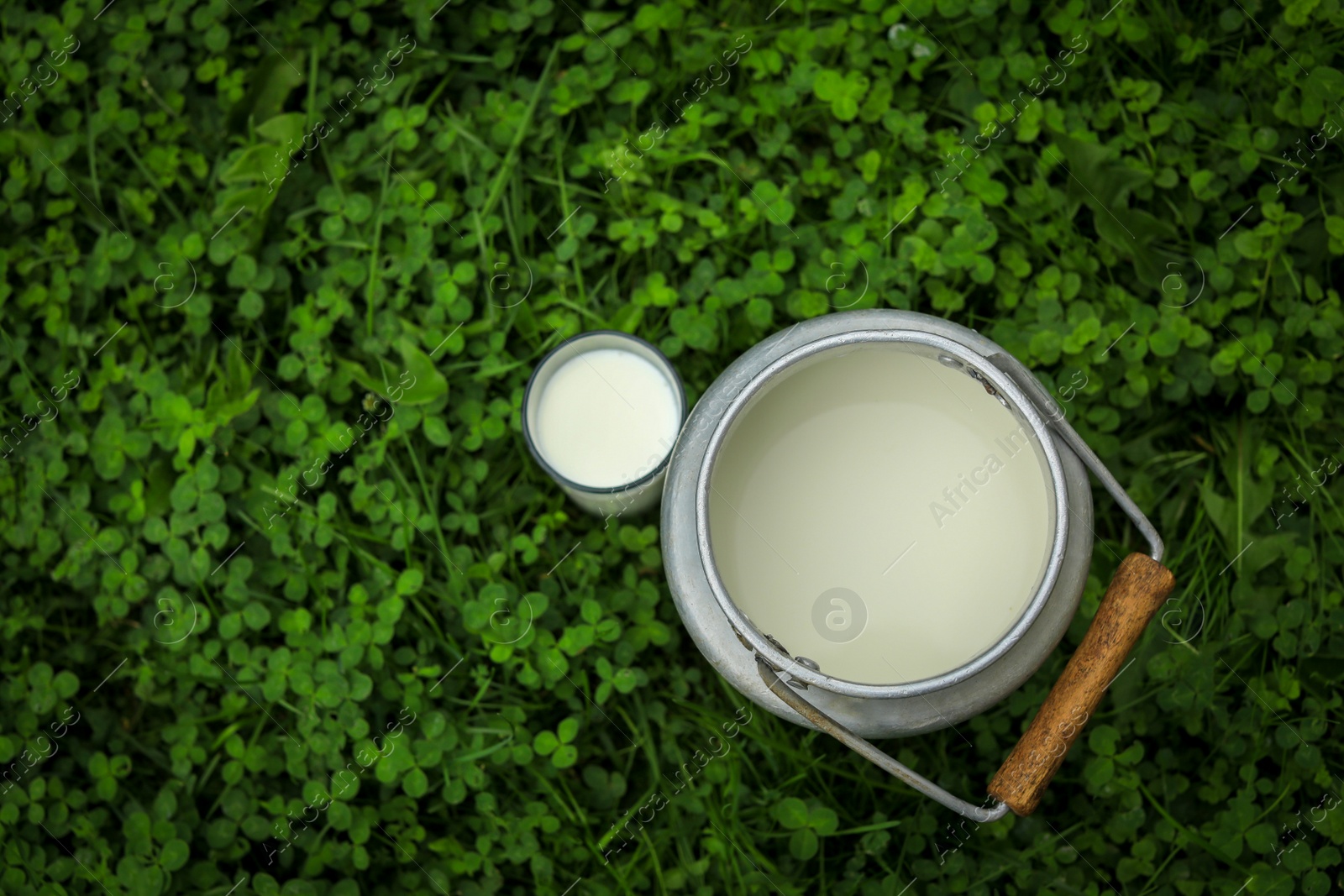 Photo of Can and glass with fresh milk on green grass outdoors, flat lay. Space for text