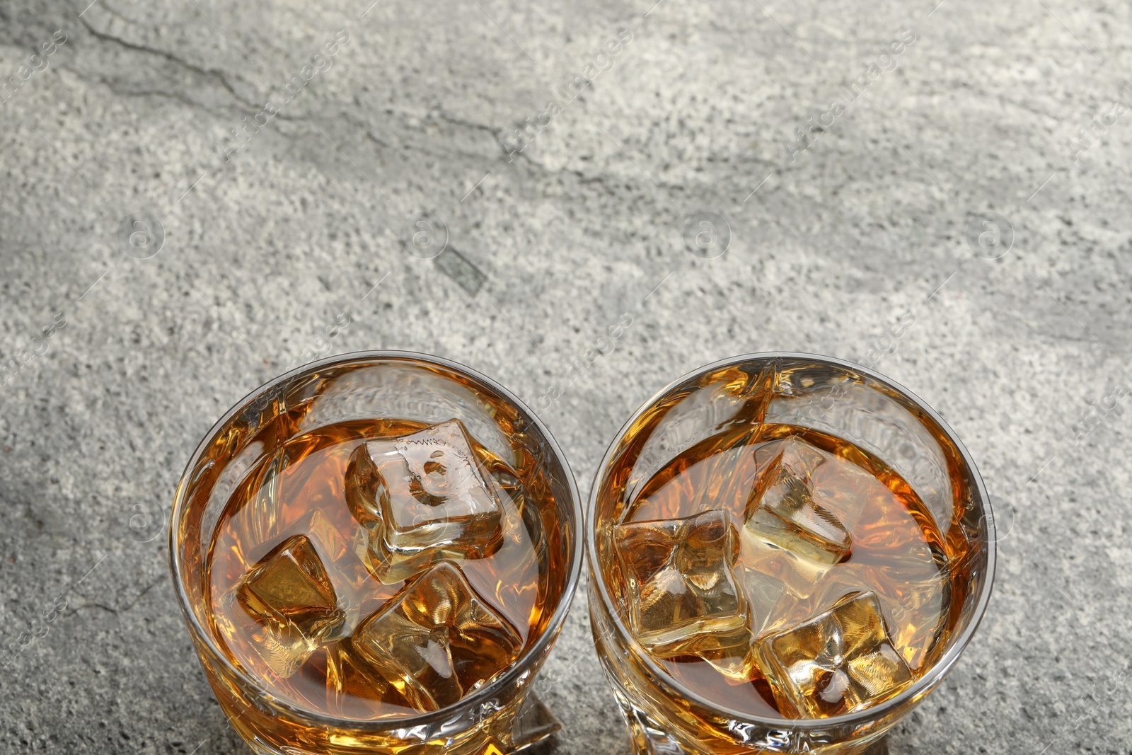 Photo of Whiskey and ice cubes in glasses on grey textured table, above view. Space for text