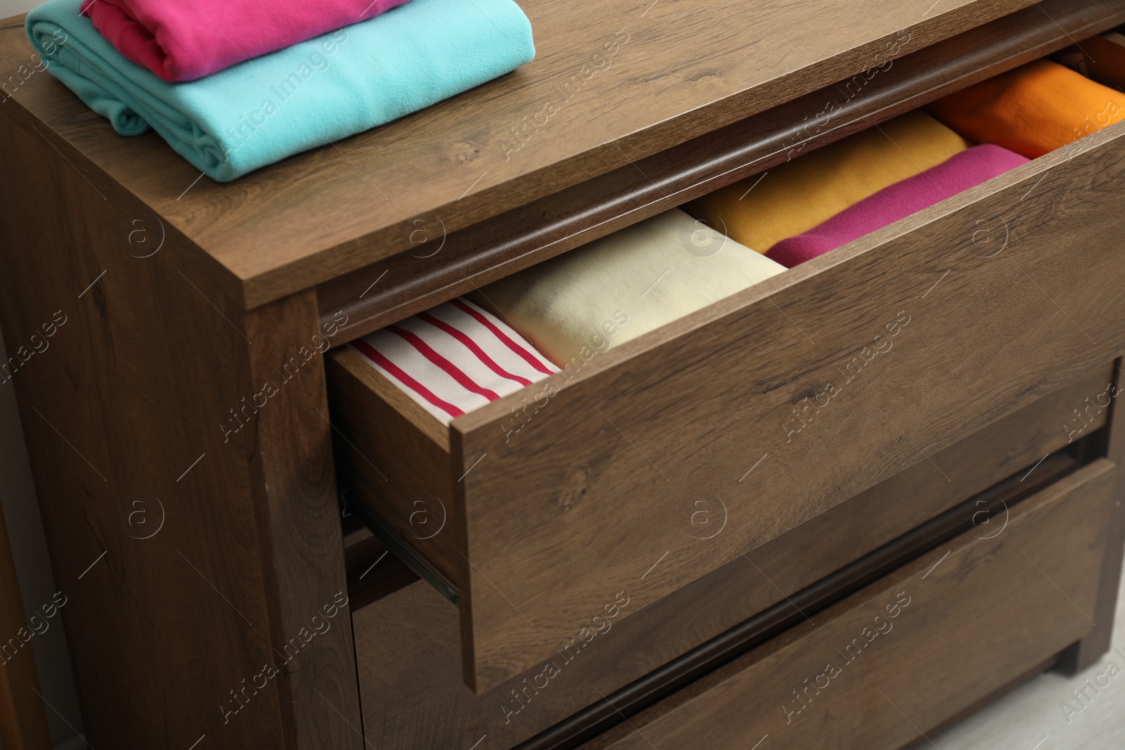 Photo of Wooden chest of drawers with different folded clothes indoors, closeup