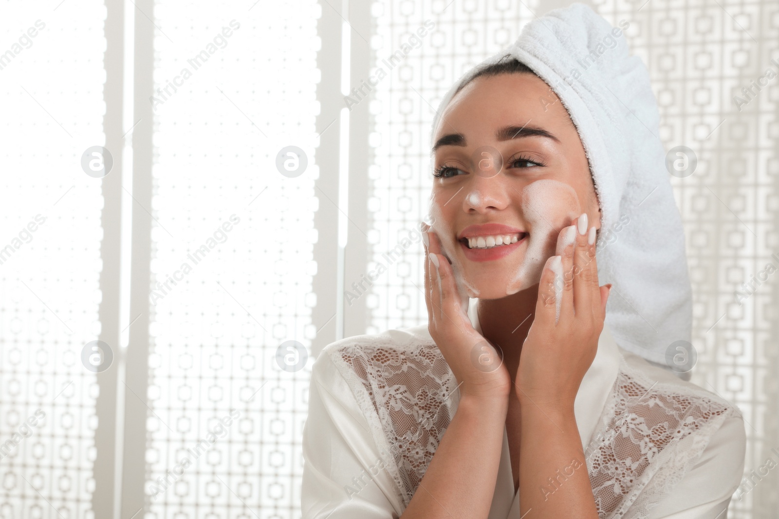 Photo of Beautiful young woman applying cleansing foam onto face in bathroom. Skin care cosmetic