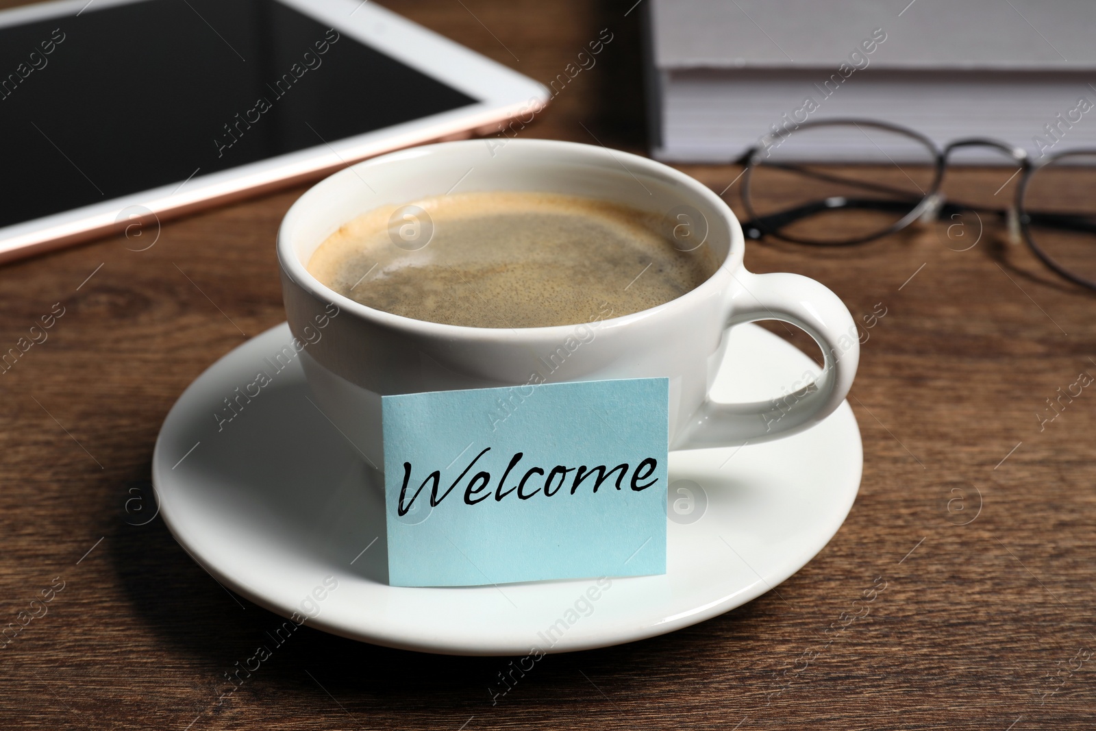 Image of Sticky note with word Welcome attached to cup of coffee on wooden office desk