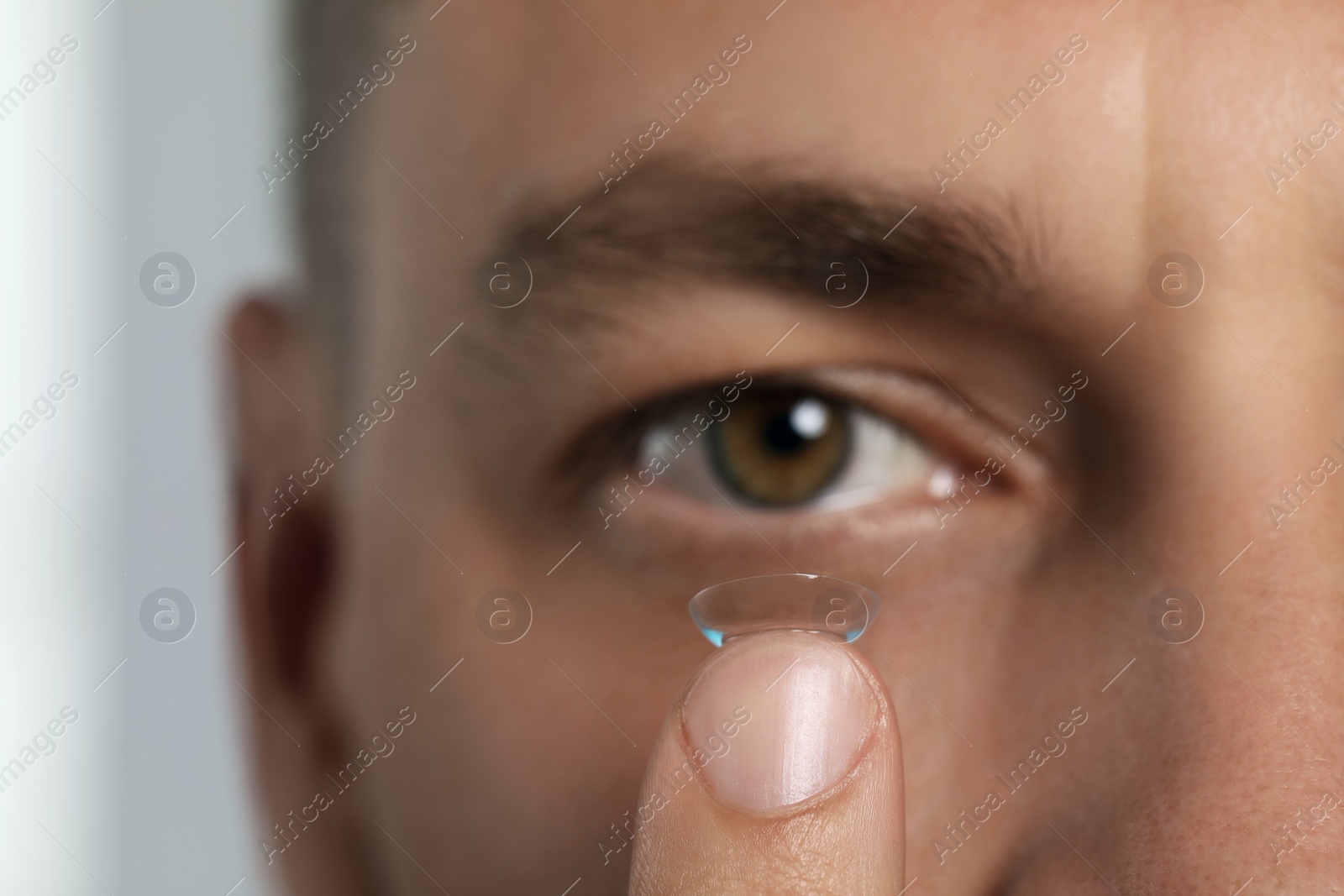 Photo of Man putting contact lens in his eye on blurred background, closeup