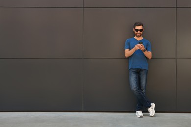 Photo of Happy man with smartphone near grey wall outdoors. Space for text