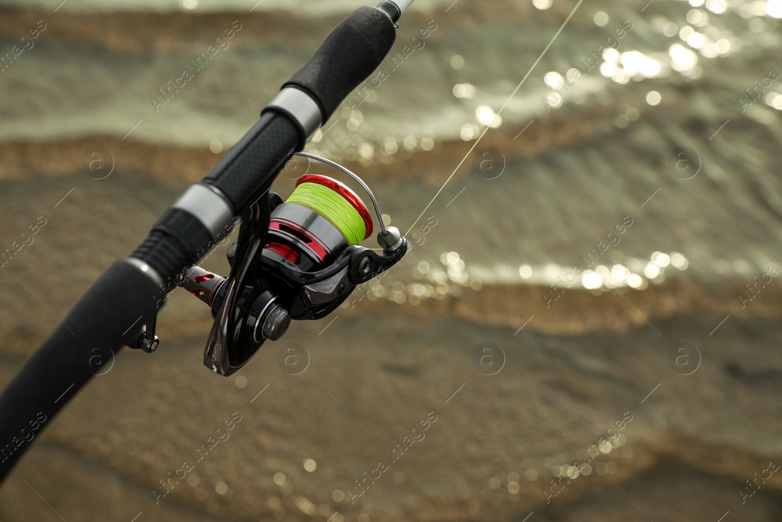 Photo of Fishing rod with reel near river, closeup. Space for text