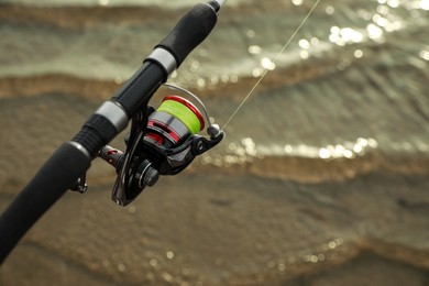 Photo of Fishing rod with reel near river, closeup. Space for text