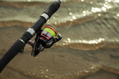 Fishing rod with reel near river, closeup. Space for text