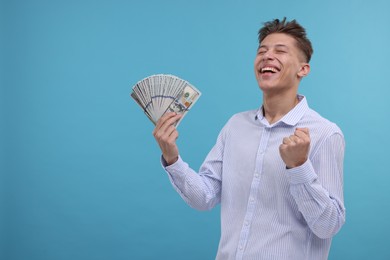 Photo of Happy man with dollar banknotes on light blue background. Space for text