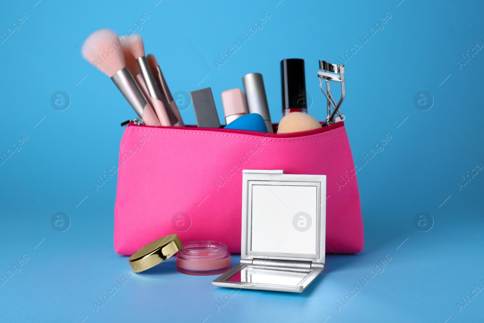 Photo of Stylish pocket mirror and cosmetic bag with makeup products on light blue background