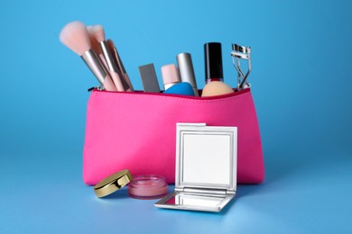 Stylish pocket mirror and cosmetic bag with makeup products on light blue background