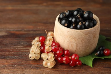 Photo of Different fresh ripe currants and green leaf on wooden table, closeup. Space for text