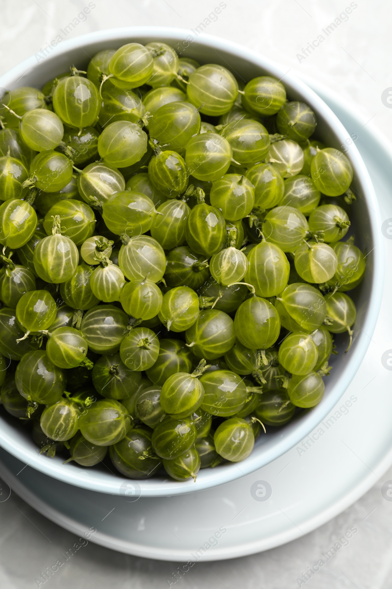 Photo of Bowl full of ripe gooseberries on light grey marble table, top view