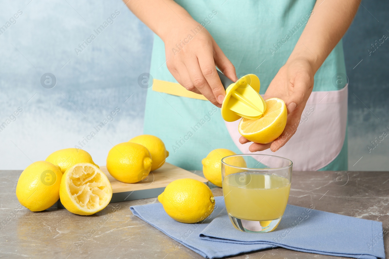 Photo of Woman squeezing lemon juice with reamer into glass on table