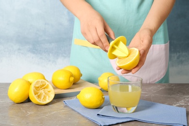 Woman squeezing lemon juice with reamer into glass on table