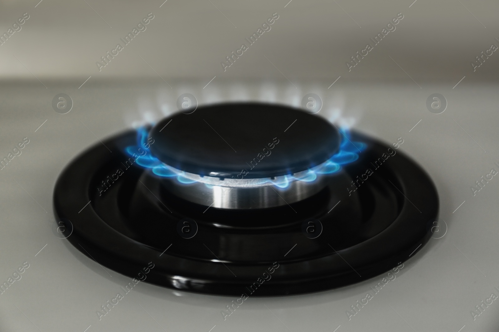 Photo of Gas burner with blue flame on modern stove, closeup