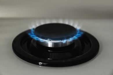 Photo of Gas burner with blue flame on modern stove, closeup