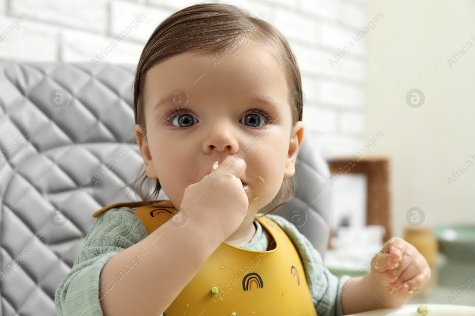 Photo of Cute little baby eating healthy food in high chair indoors