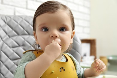 Cute little baby eating healthy food in high chair indoors