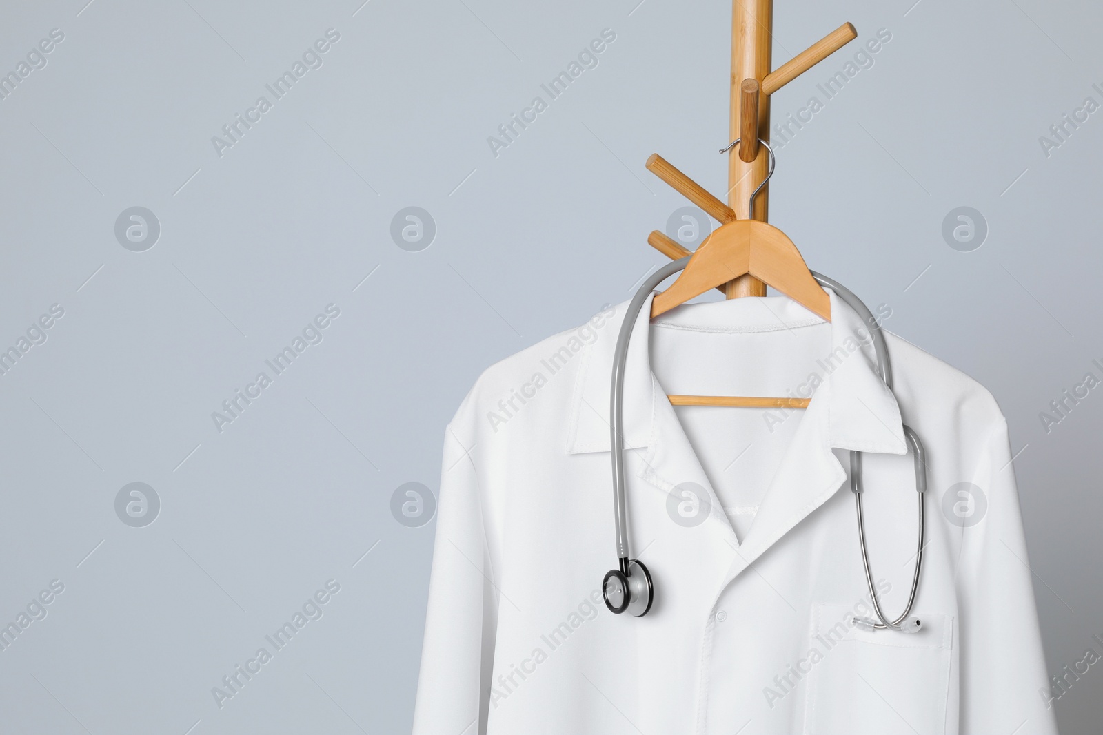 Photo of Medical uniform and stethoscope hanging on rack against light grey background. Space for text