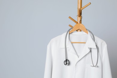 Photo of Medical uniform and stethoscope hanging on rack against light grey background. Space for text