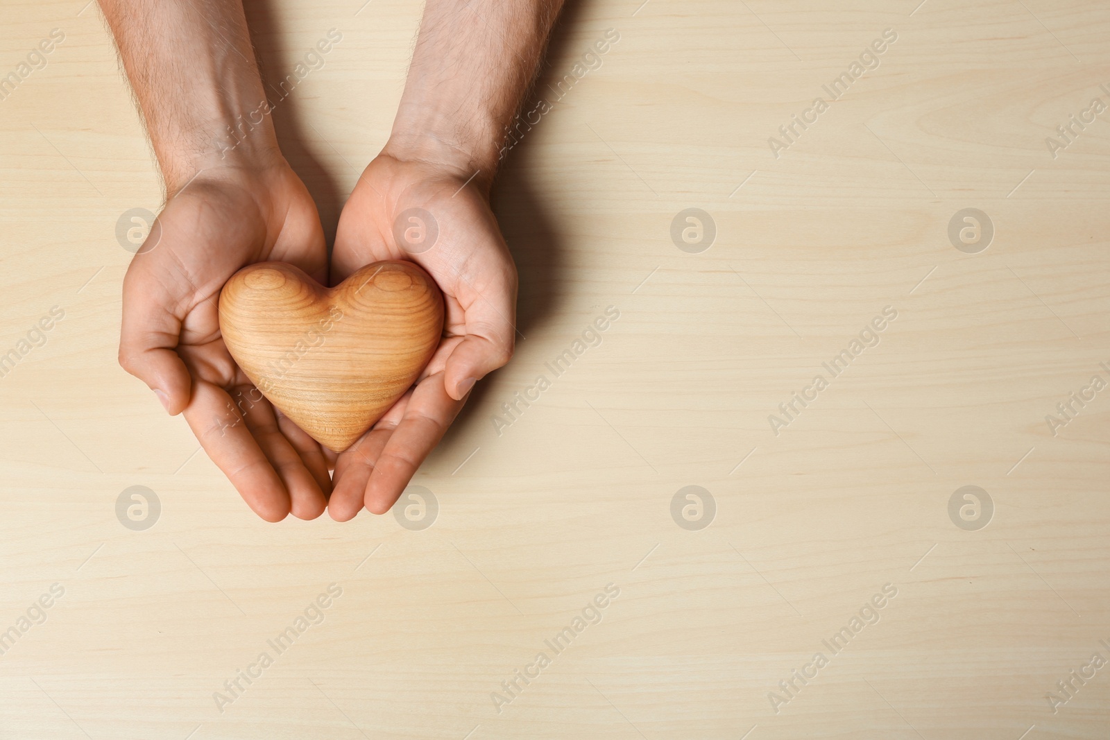 Photo of Young man holding heart on light wooden background, top view with space for text. Donation concept