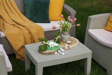 Easter decorations. Bouquet of tulips in vase, bunny figures and decorated eggs on table in backyard