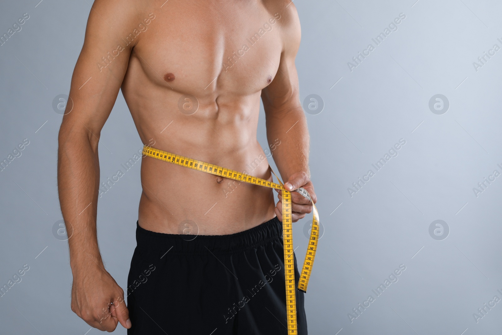 Photo of Shirtless man with slim body and measuring tape around his waist on grey background, closeup. Space for text