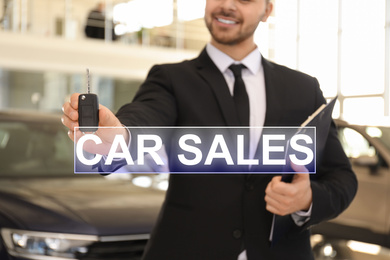 Image of Salesman with key and clipboard in car dealership, closeup