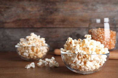 Photo of Glass bowl with tasty popcorn on table. Space for text