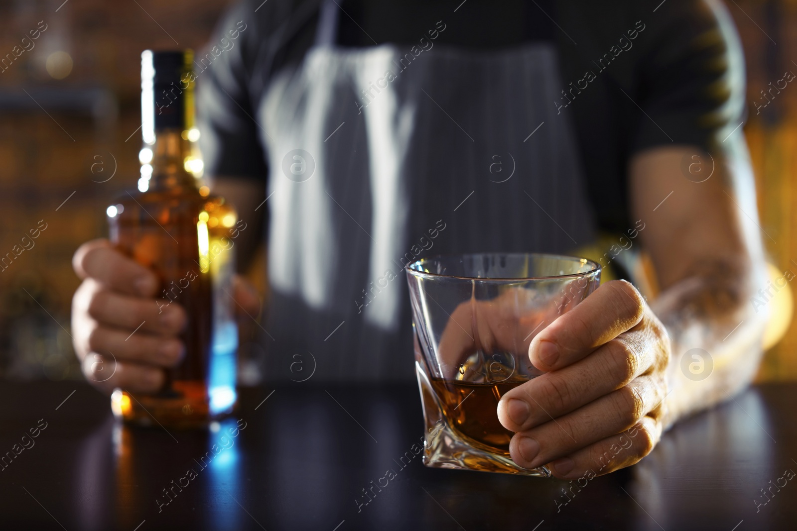 Photo of Bartender with glass and bottle of whiskey at counter in bar, closeup. Space for text