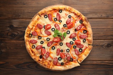 Photo of Tasty pizza with dry smoked sausages, tomato, olives, pepper and parsley on wooden table, top view