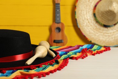 Black Flamenco hat, poncho and maracas on light wooden table, closeup. Space for text