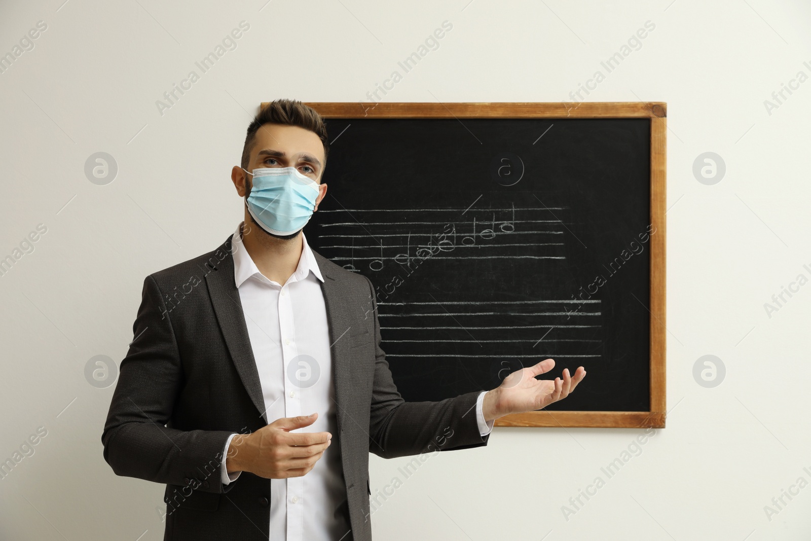 Photo of Teacher wearing protective mask near black chalkboard with music notes in classroom