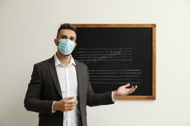 Photo of Teacher wearing protective mask near black chalkboard with music notes in classroom