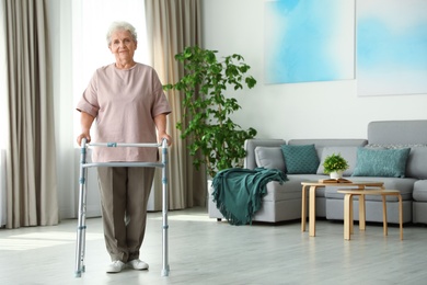 Photo of Elderly woman using walking frame indoors. Space for text