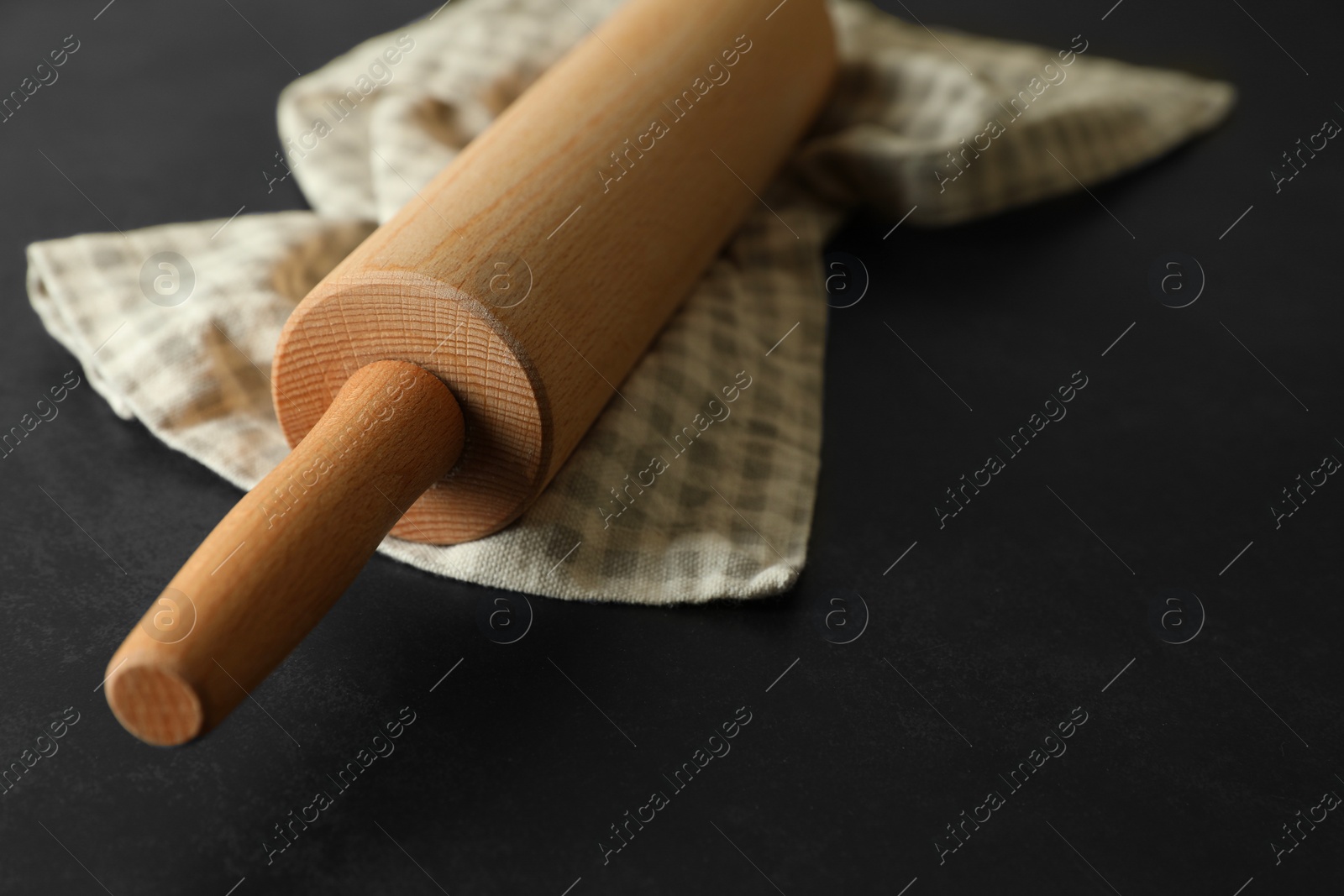 Photo of Rolling pin and kitchen towel on black table, closeup. Space for text