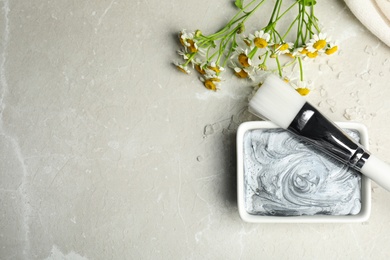 Photo of Professional face mask with brush and flowers on light gray marble table, flat lay. Space for text