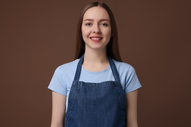 Beautiful young woman wearing kitchen apron on brown background. Mockup for design