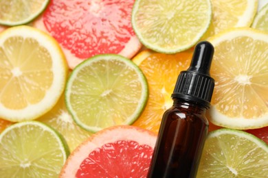 Photo of Bottle of essential oil on pile of citrus slices, flat lay. Space for text