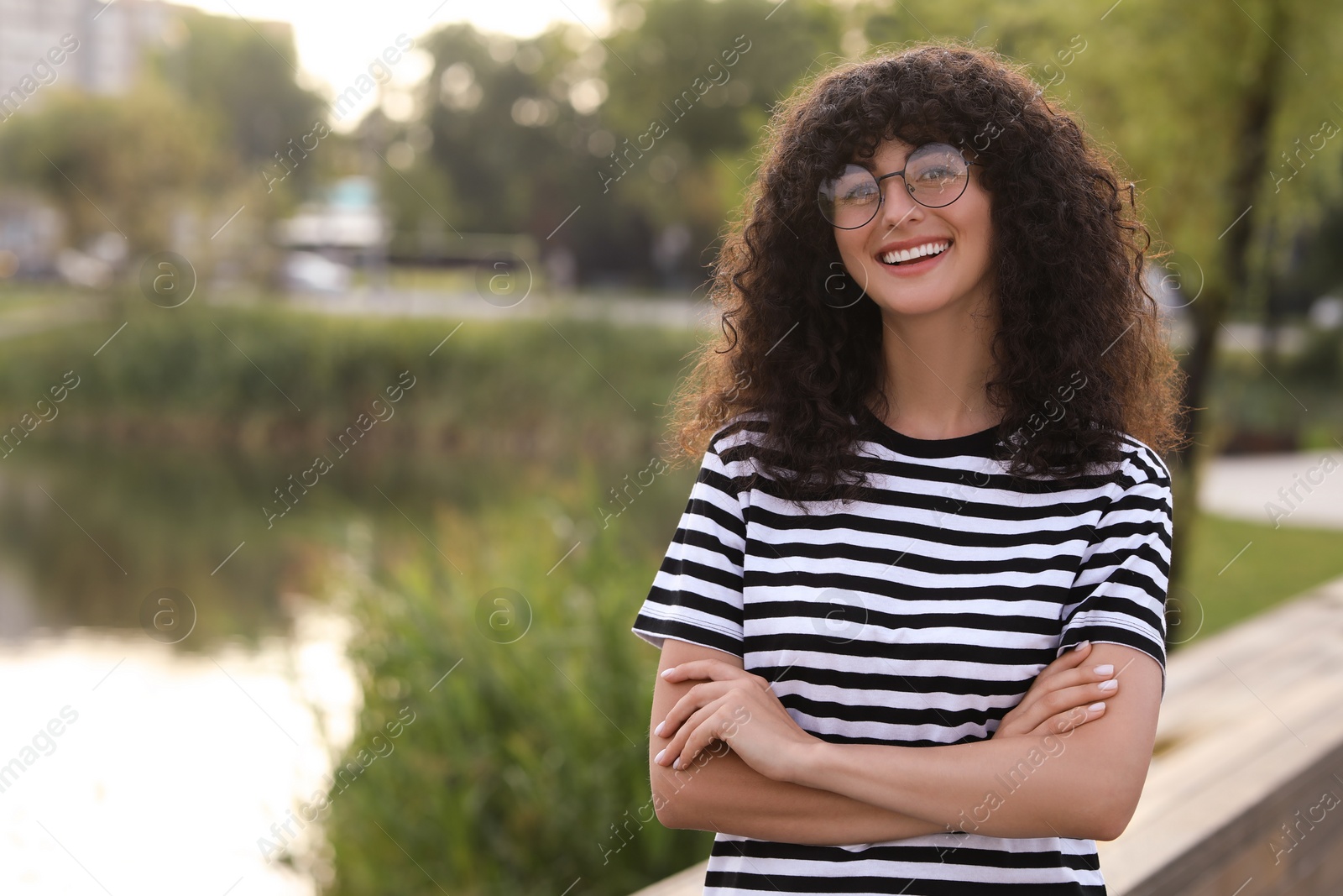 Photo of Portrait of beautiful woman in glasses with crossed arms outdoors. Attractive lady smiling and looking into camera. Space for text