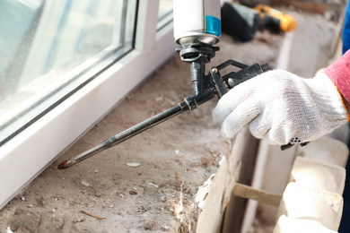 Photo of Worker using foam gun for window installation indoors, closeup