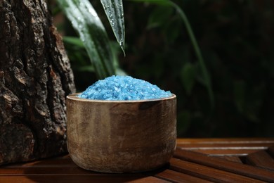 Photo of Bowl of blue sea salt on wooden table, closeup. Space for text