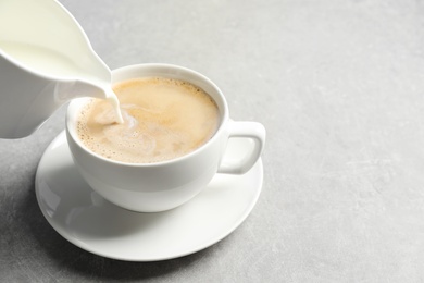 Photo of Pouring milk into cup of hot coffee on grey table, space for text