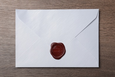Photo of White envelope with wax seal on wooden table, top view