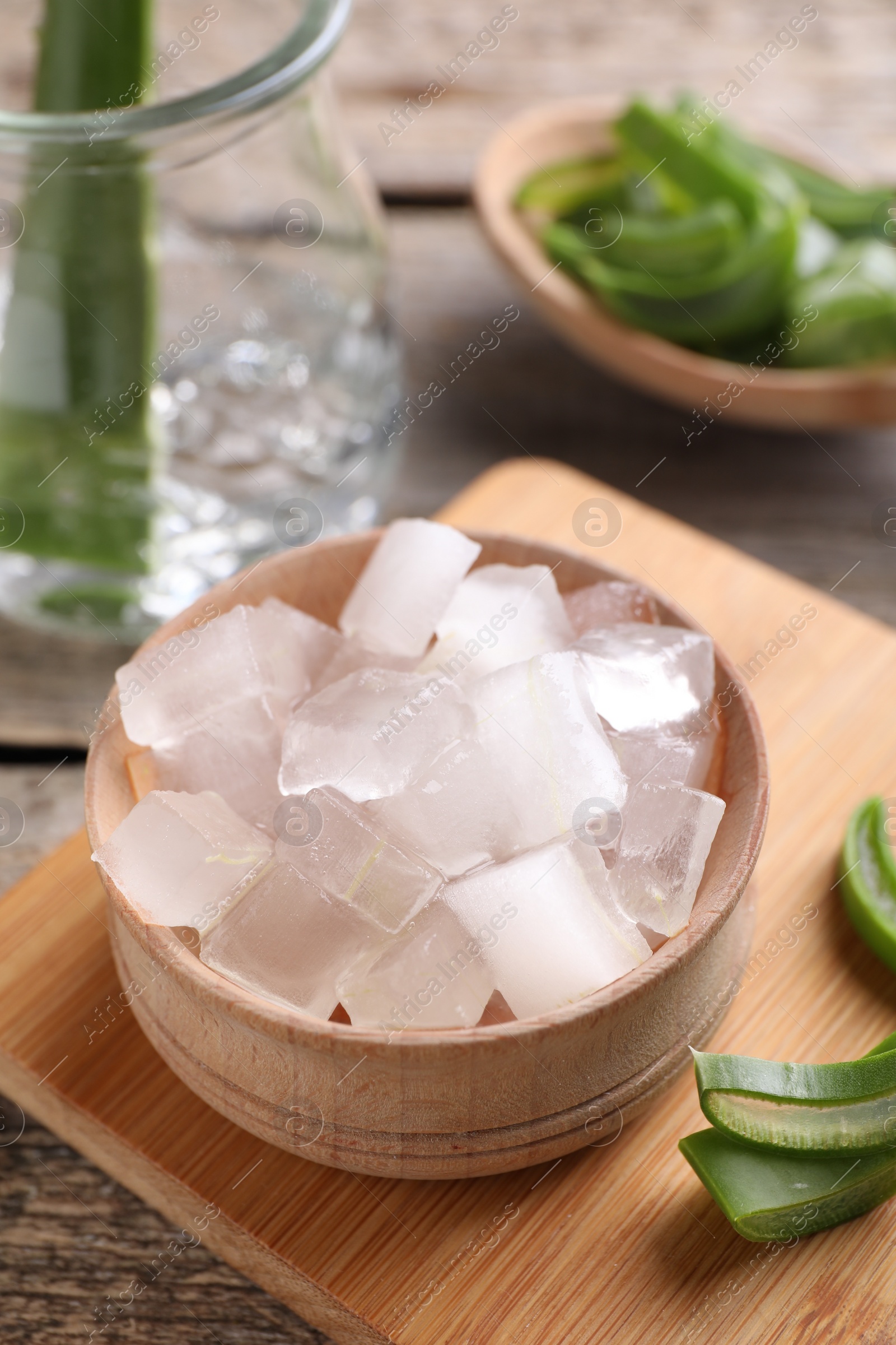 Photo of Aloe vera gel and slices of plant on wooden table, closeup